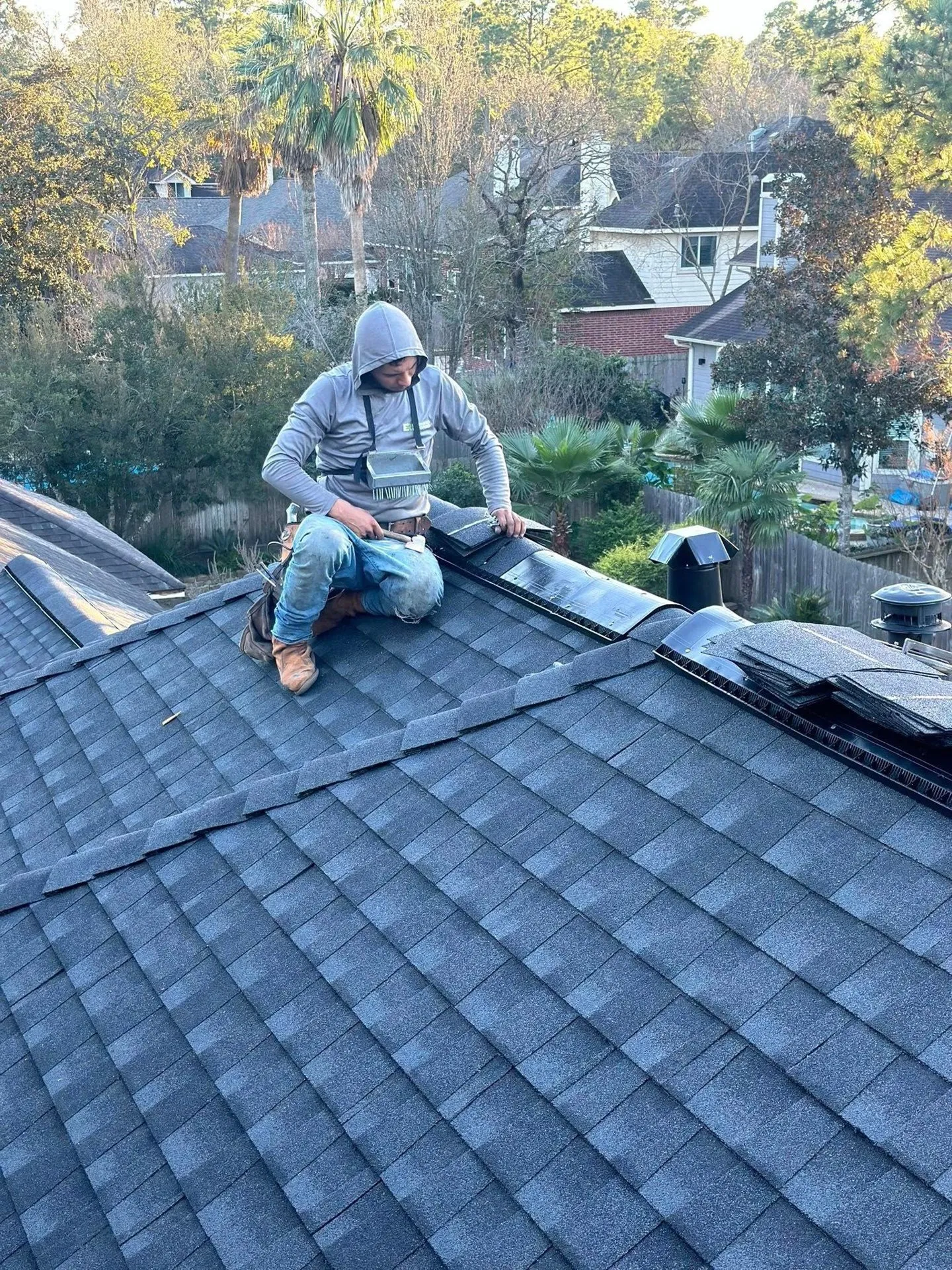 An Entrusted Roofing crew member working on a dark shingle roof